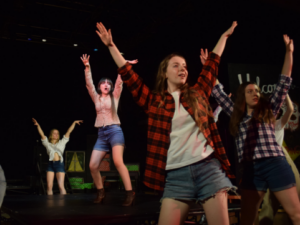 Photograph of students performing in the Footloose production with their hands in the air.