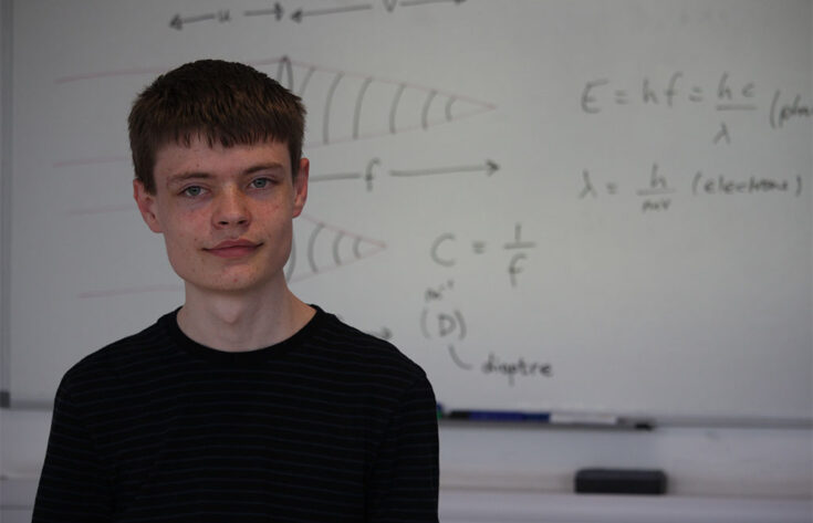 Photograph of a physics student stood in front of a whiteboard.