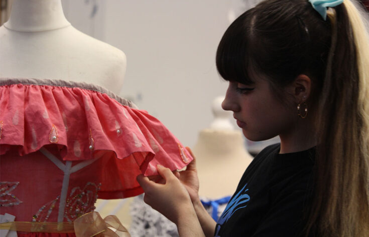 Photograph of a textiles student standing next to a dress she has made.