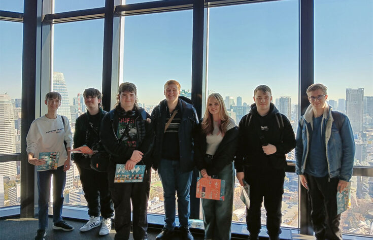 Photograph of students stood outside a window of a skyscraper